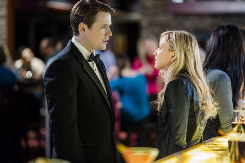 In a still from "Love on the Sidelines", Laurel and the football player stand face to face next to a bar. 