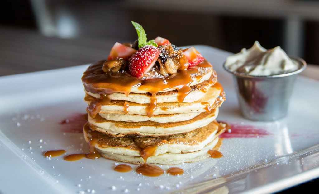A stack of pancakes covered in caramel sauce, fruit, and powdered sugar. 