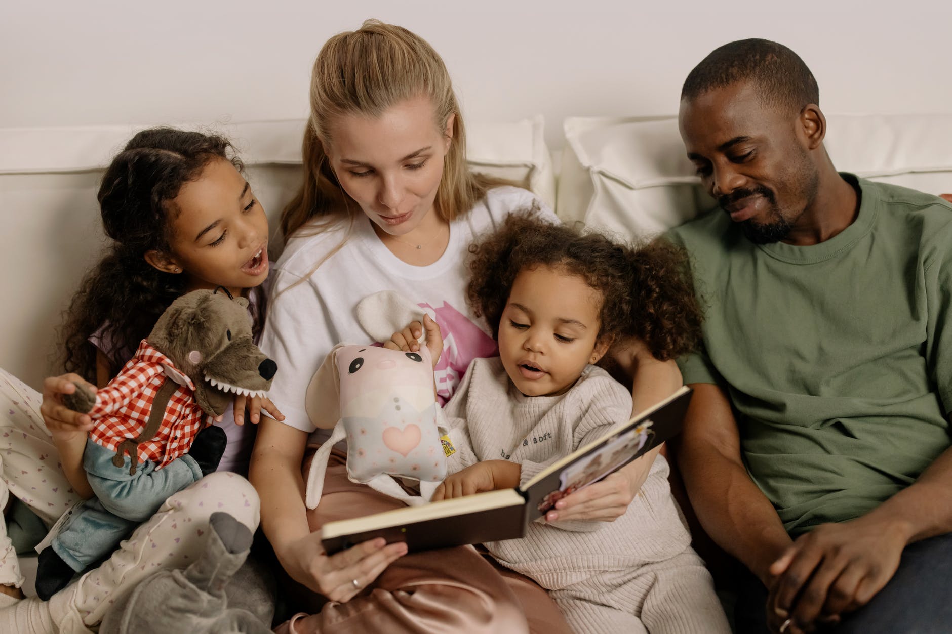 Biracial family sits on couch, reading a photobook of memories. 