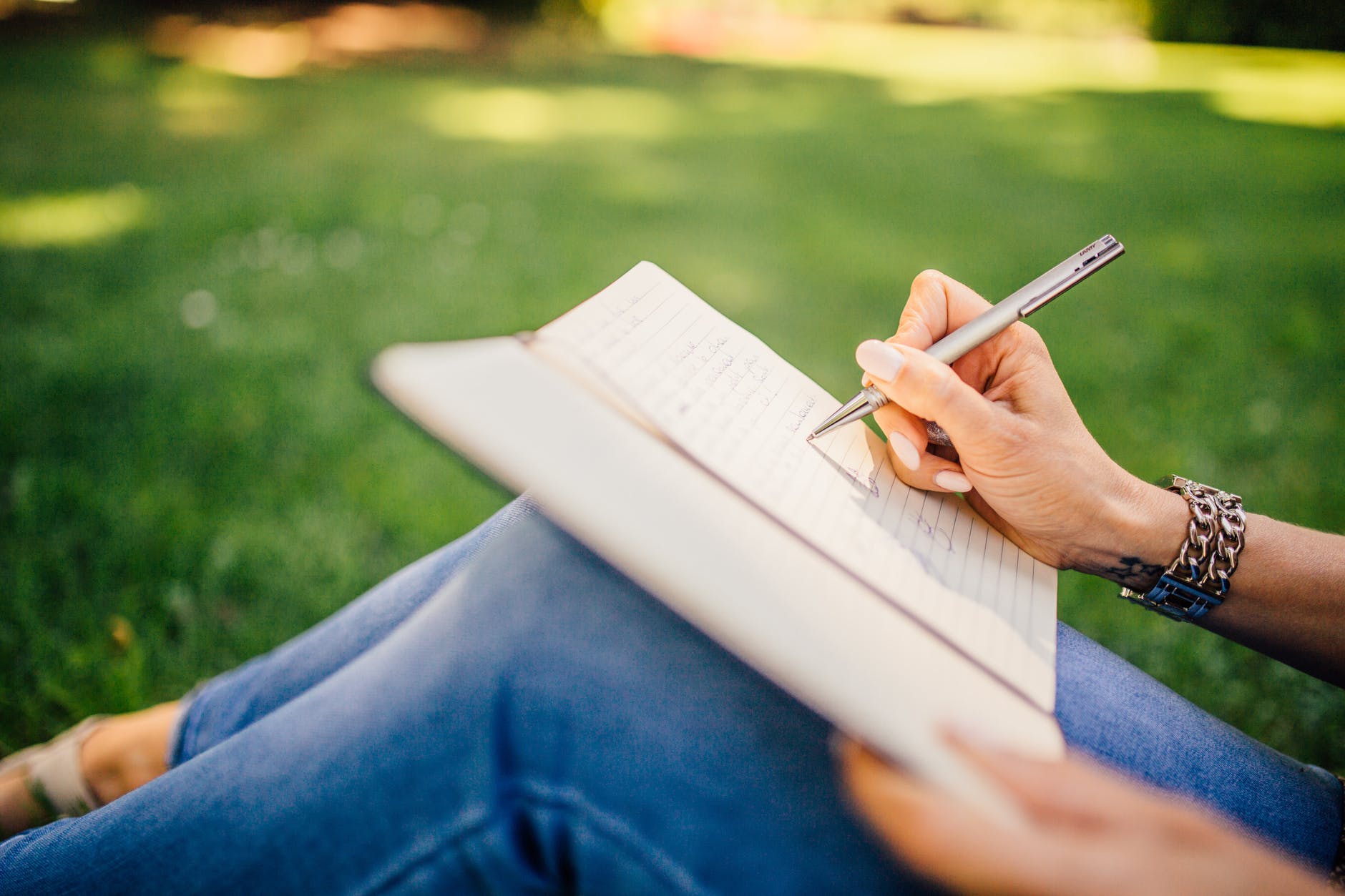 Woman sits on grass, writing about her future in a journal.